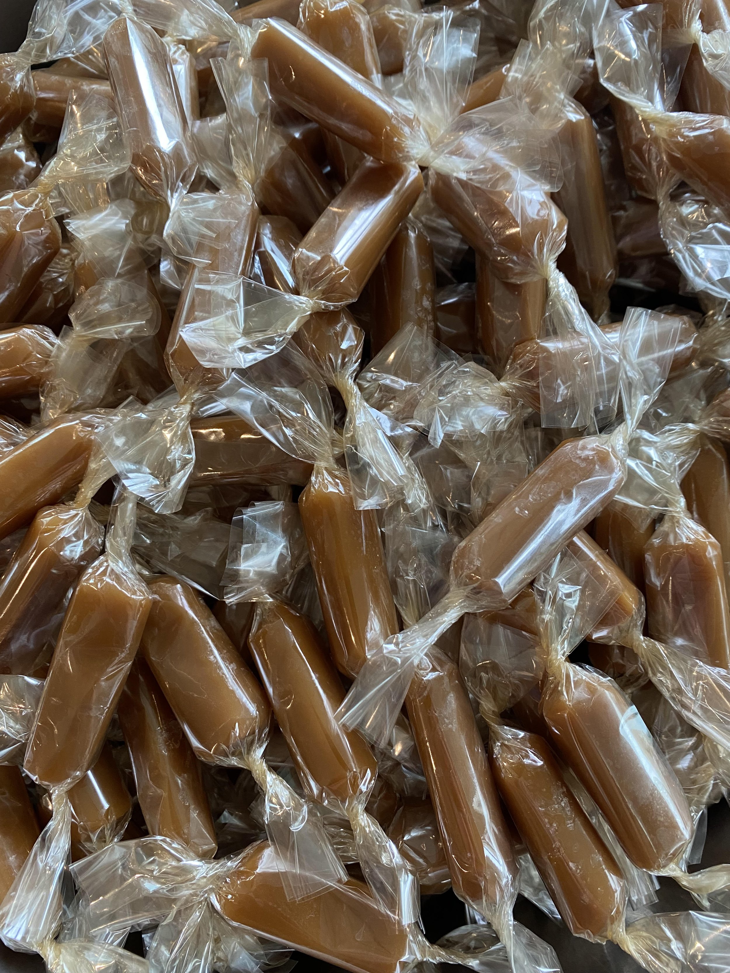A pile of individually wrapped caramel candies in clear plastic wrappers.