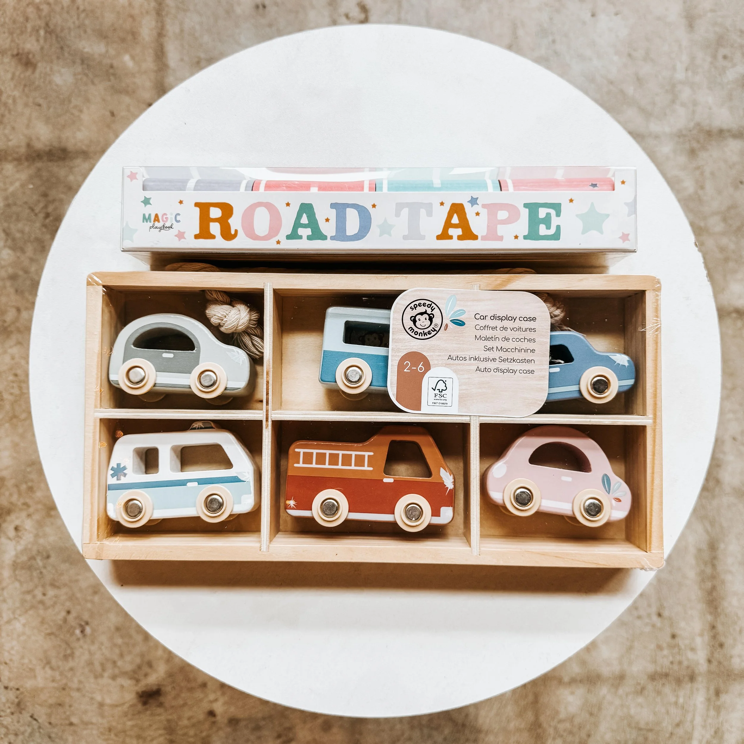 Set of six wooden toy cars in a wooden display case, colorful and designed for children aged 2 to 6, placed on a white round table.