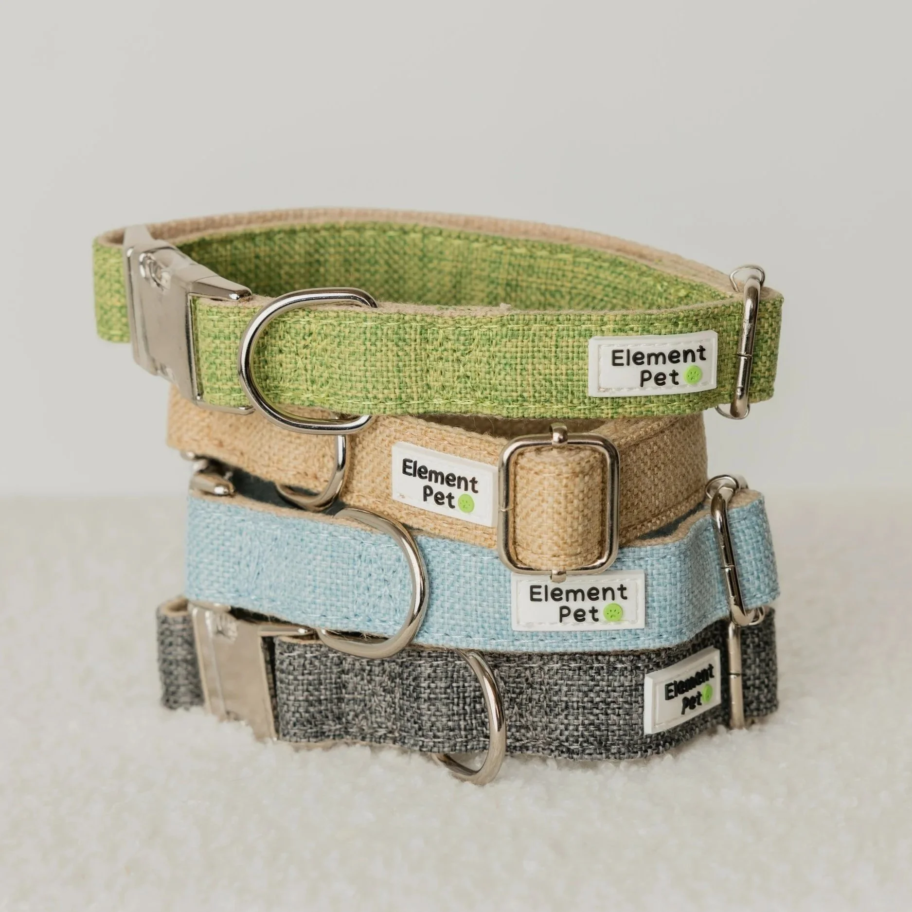Stacked colorful fabric pet collars with metal buckles and rings, labeled 'Element Pet' with small green smiley face stickers.
