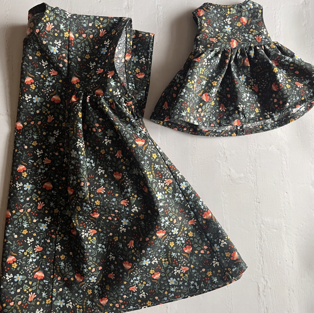 Two pieces of fabric or clothing with a black background and colorful floral pattern, one appears to be a dress or skirt with gathered fabric, and the other looks like a skirt or dress with a waistband and flared hem.