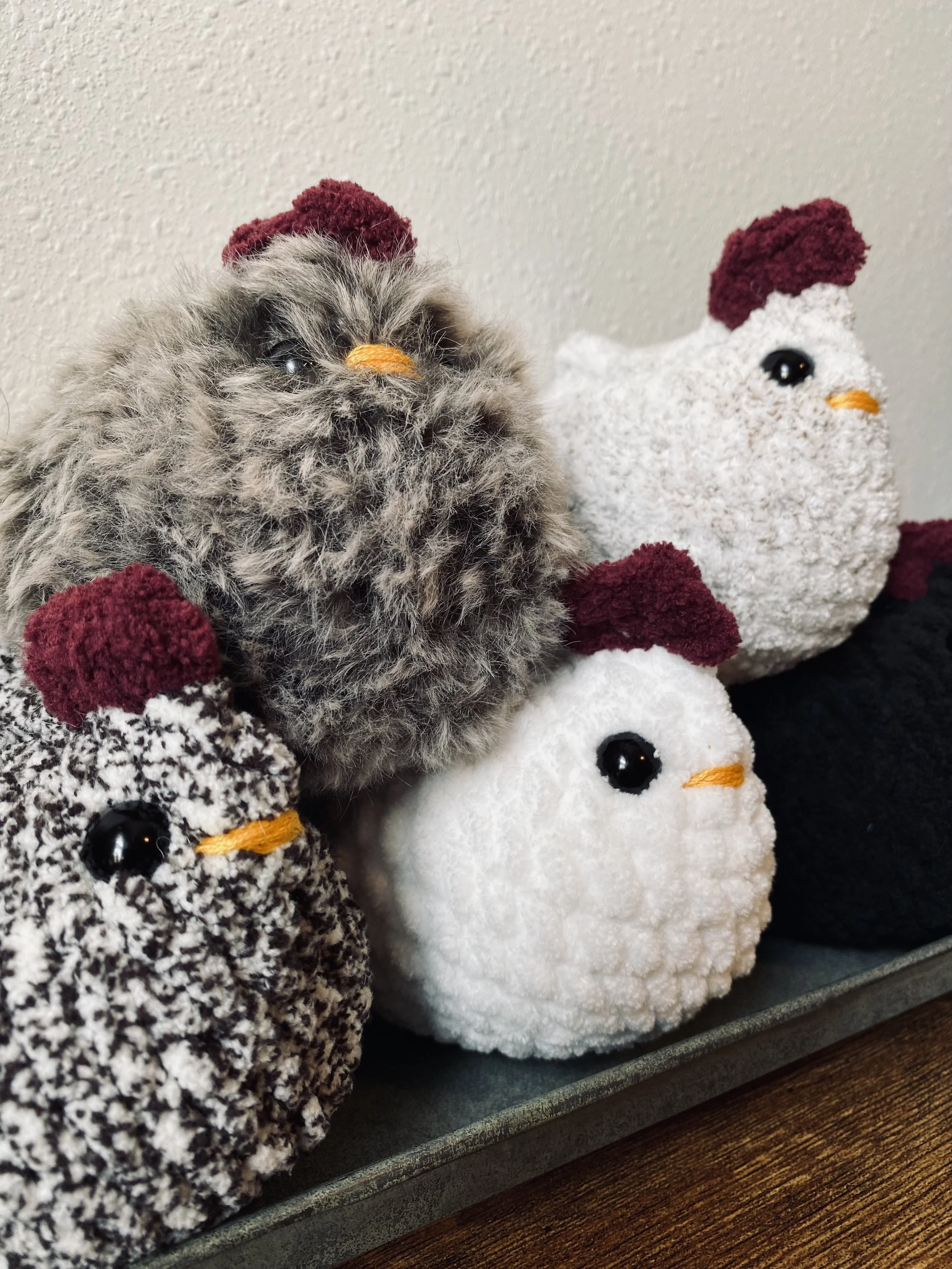 A furry chicken plush toy and three egg-shaped plush toys with red combs, black eyes, and yellow beaks, placed on a surface against a plain wall.