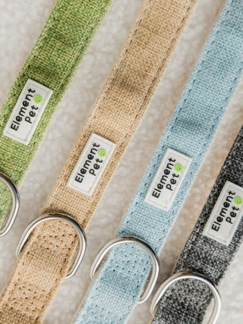 Four colorful fabric pet collars with metal D-rings, arranged diagonally. Each collar has a label that reads 'Element Pet' with a small green paw print.