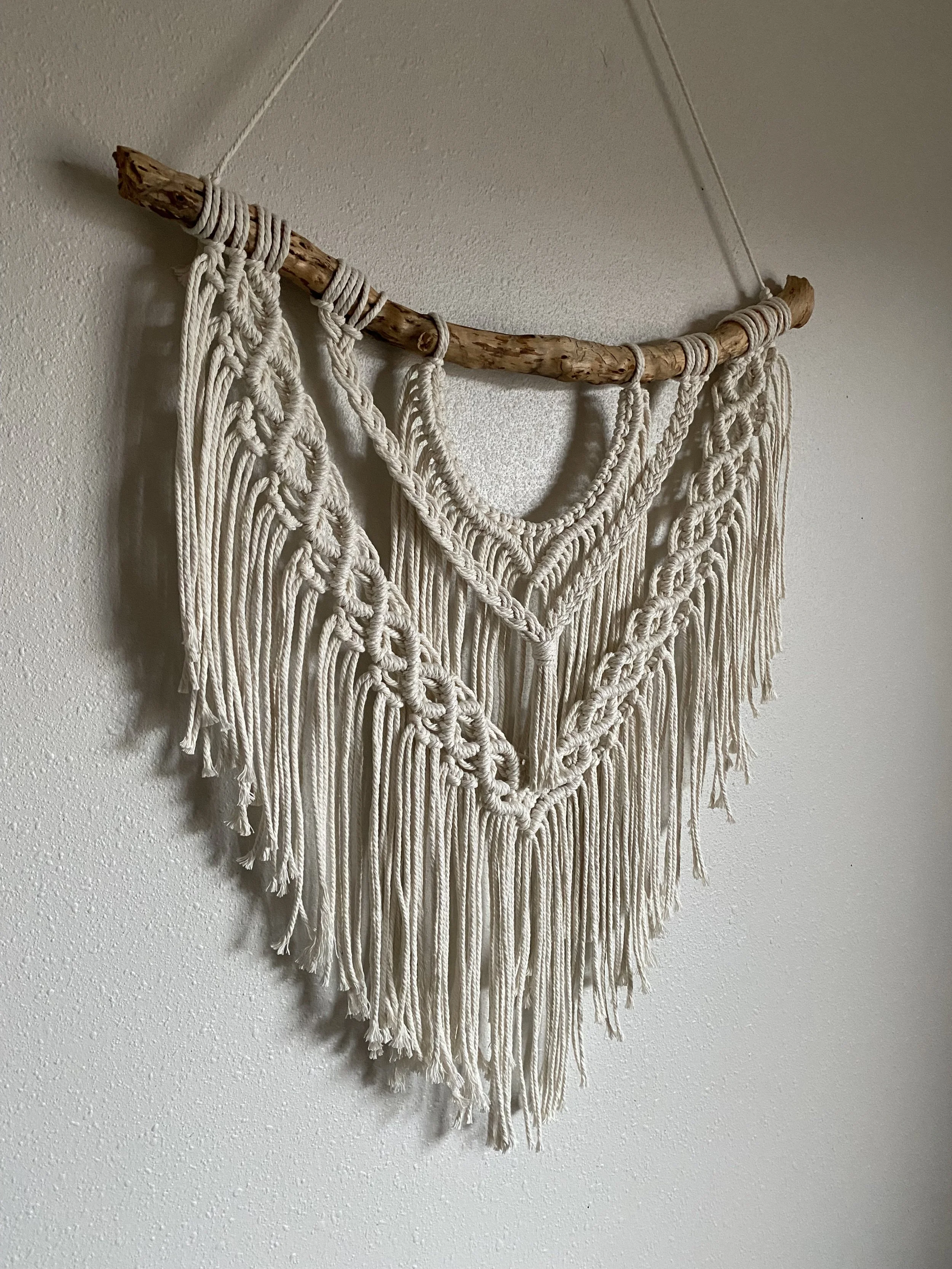 Macrame wall hanging with cream-colored cords and a wooden branch