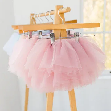Pink tutu skirts hanging on a wooden clothing rack near a window.