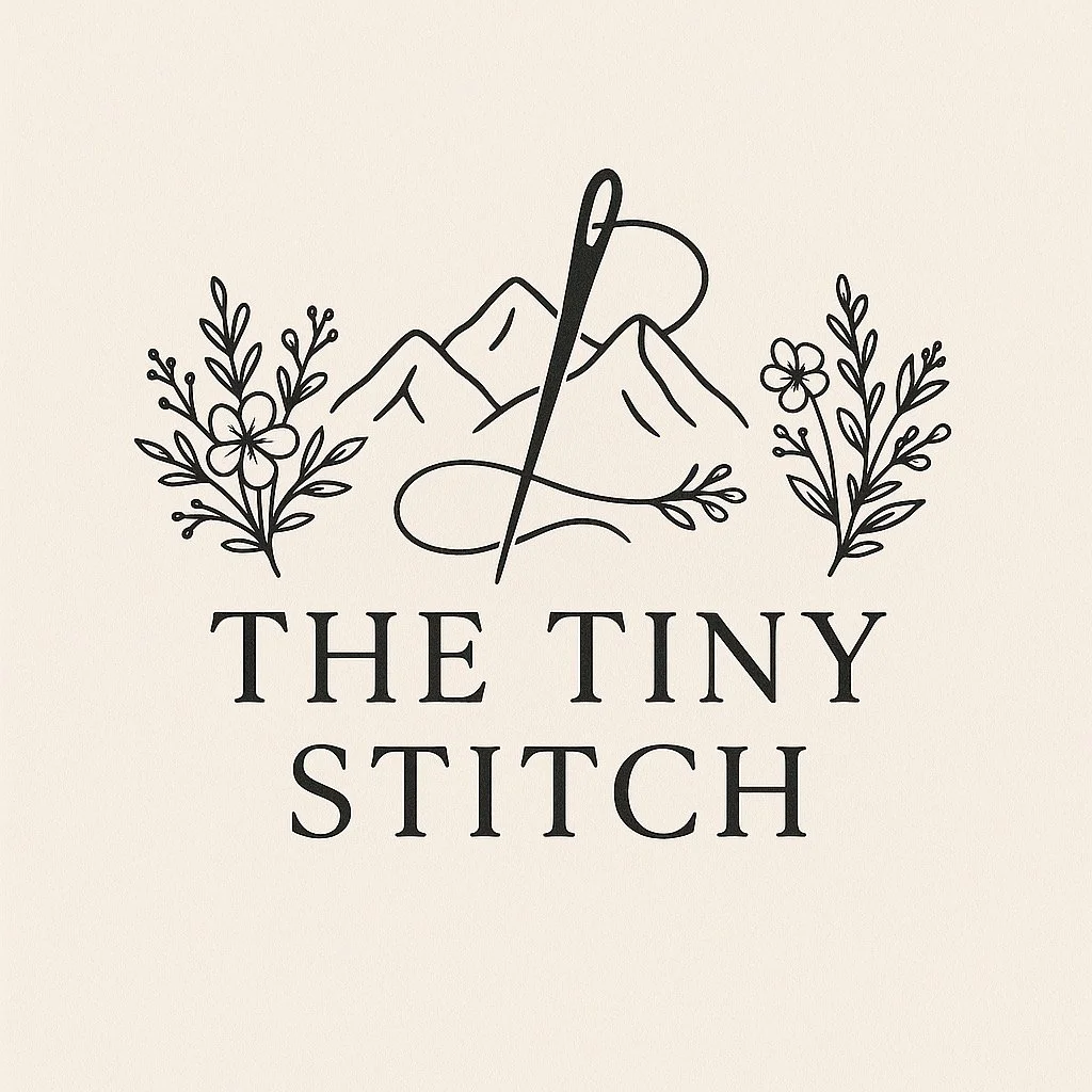 A minimal black and white logo featuring a mountain range, a sewing needle with thread, and two floral arrangements on either side. Below, the text reads 'The Tiny Stitch'.
