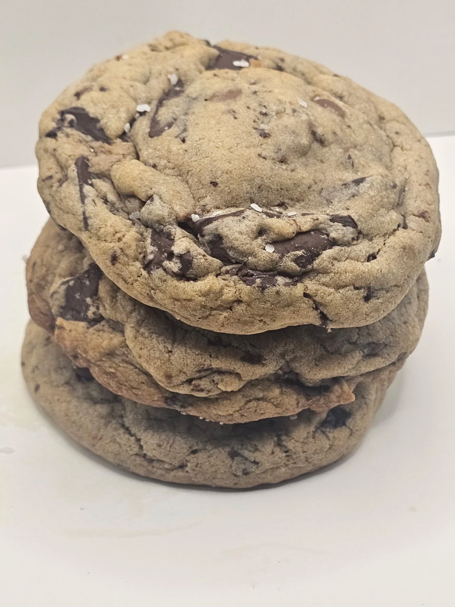 Three stacked chocolate chip cookies on a white surface.