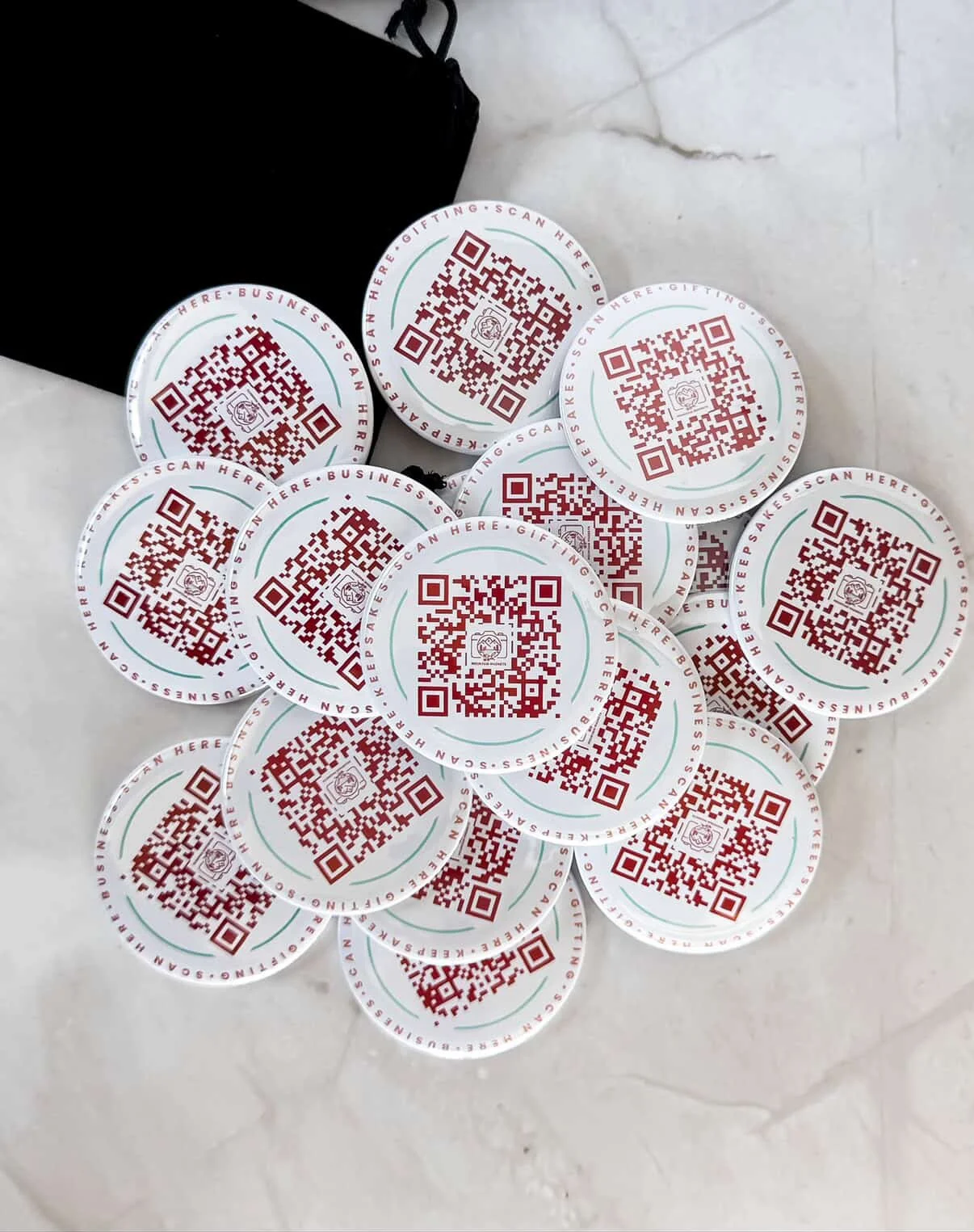 Multiple round stickers with QR codes on a white surface near a black bag.
