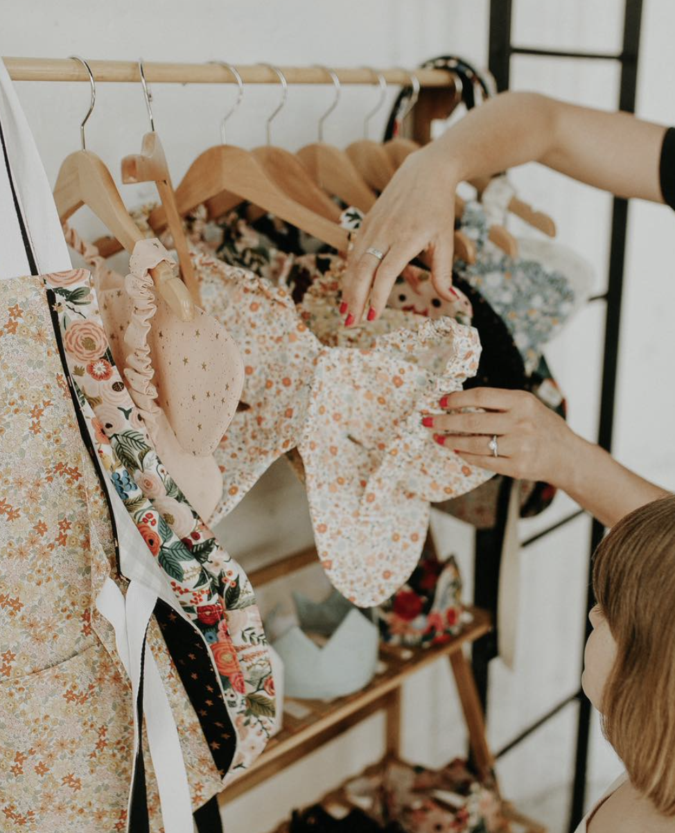Person and child looking at floral-patterned clothing on a rack, with hand picking out a garment.