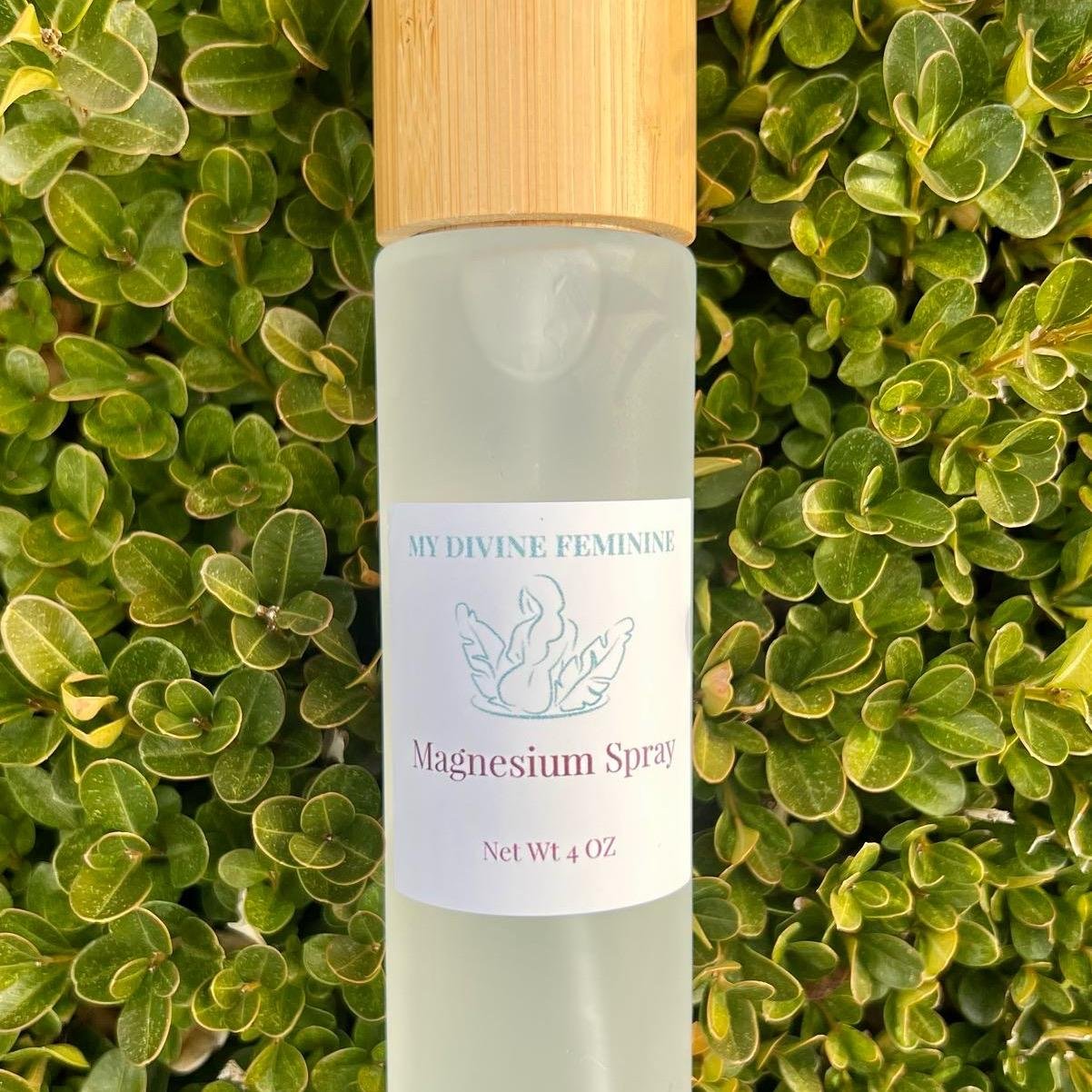 A bottle of My Divine Feminine Magnesium Spray with a light wooden cap, positioned against a backdrop of green, leafy foliage.
