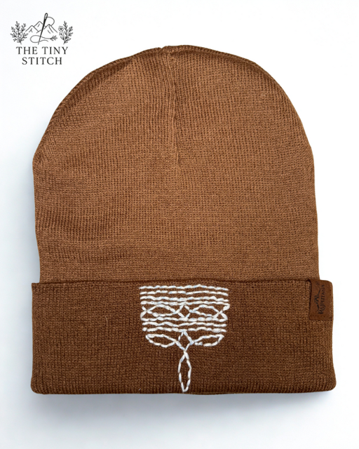Brown knit beanie hat with embroidered white tree design on the front cuff.