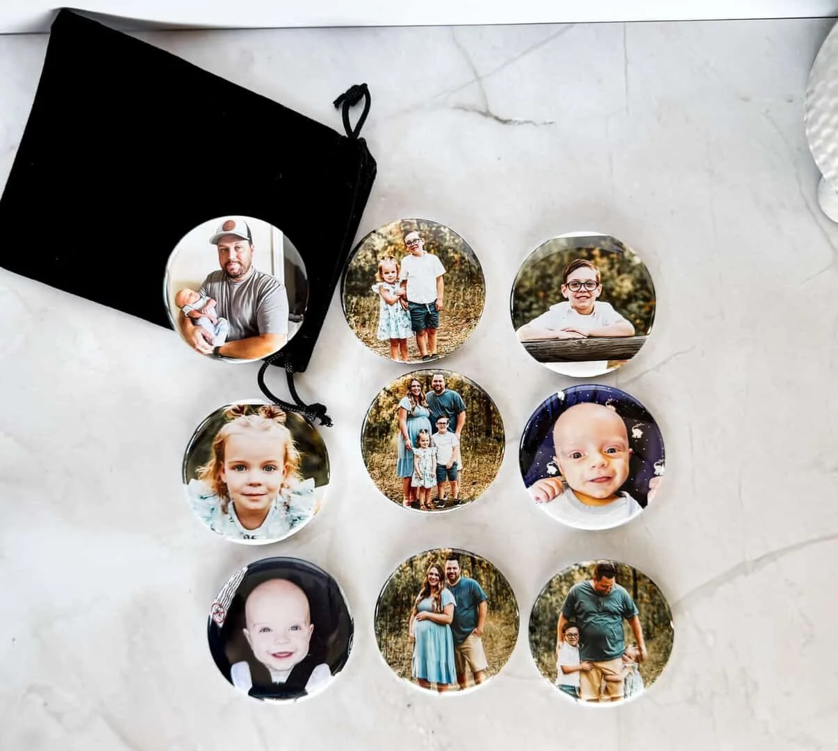 Set of round photo buttons featuring family photos, placed on a white surface with a black pouch nearby.