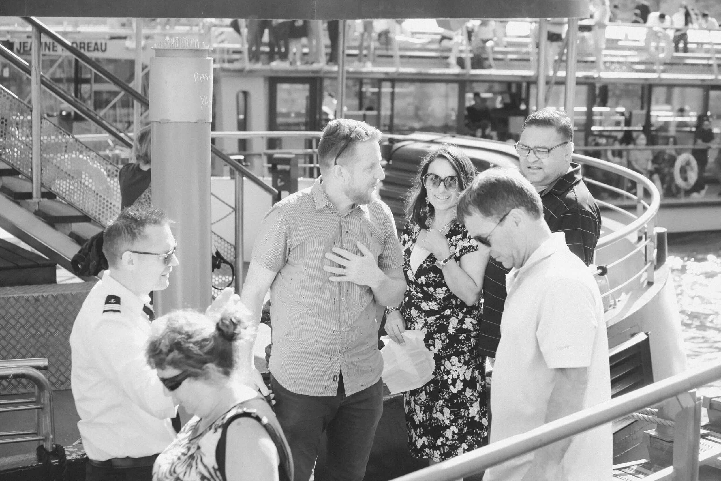 Group of people on a ferry dock, some engaged in conversation, with a watercraft in the background.