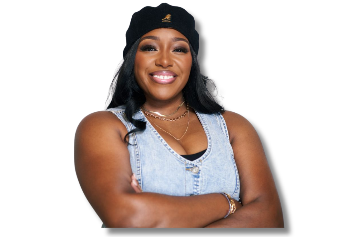 A woman with dark hair wearing a black beanie, a denim sleeveless vest, and gold jewelry, smiling with arms crossed