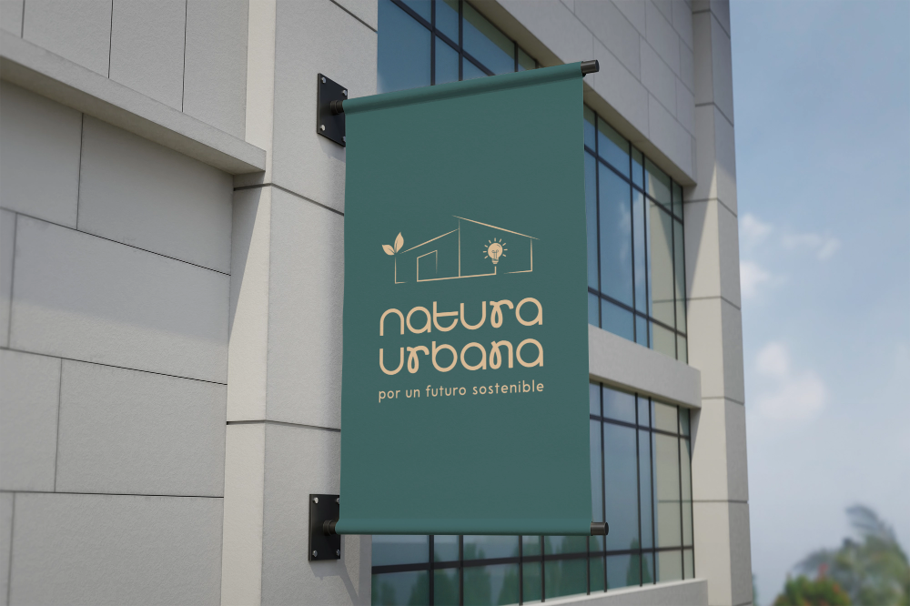 A green vertical banner on an exterior wall of a modern building with large glass windows. The banner displays a logo of a house with a leaf and sun, and text that reads "natur a urbana" and "por un futuro sostenible."