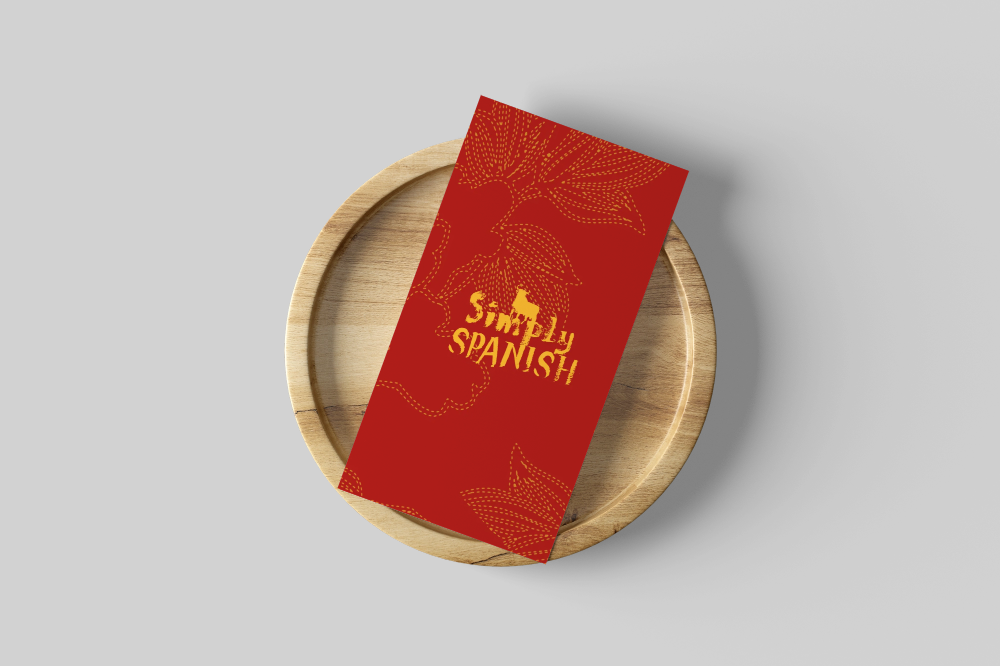 Red booklet titled 'Simply Spanish' resting on a round wooden tray with a gray background.