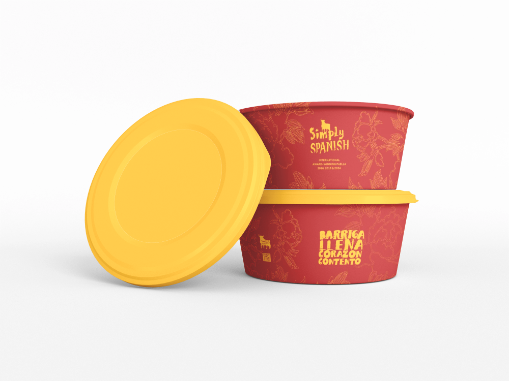 Two red containers with yellow lids, one open, with the words "Simply Spanish" and "Barriga Llena Corazón Contento" written on them. The containers are designed for food, likely takeout.