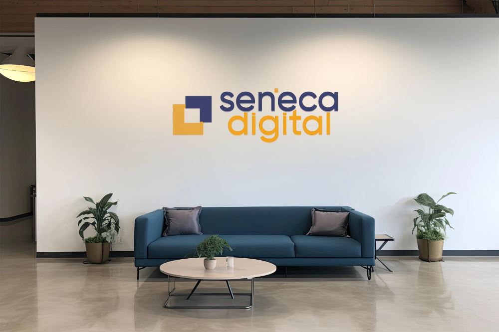 Lobby area with a blue sofa, potted plants, and a wall sign that reads "seneca digital" in bold letters.