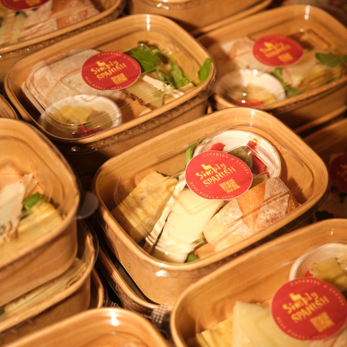 Several takeout containers labeled "Simply Spanish" filled with food, including bread, cheese, olives, and vegetables.