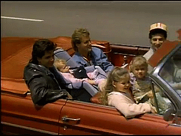Vintage convertible carrying passengers through a city street