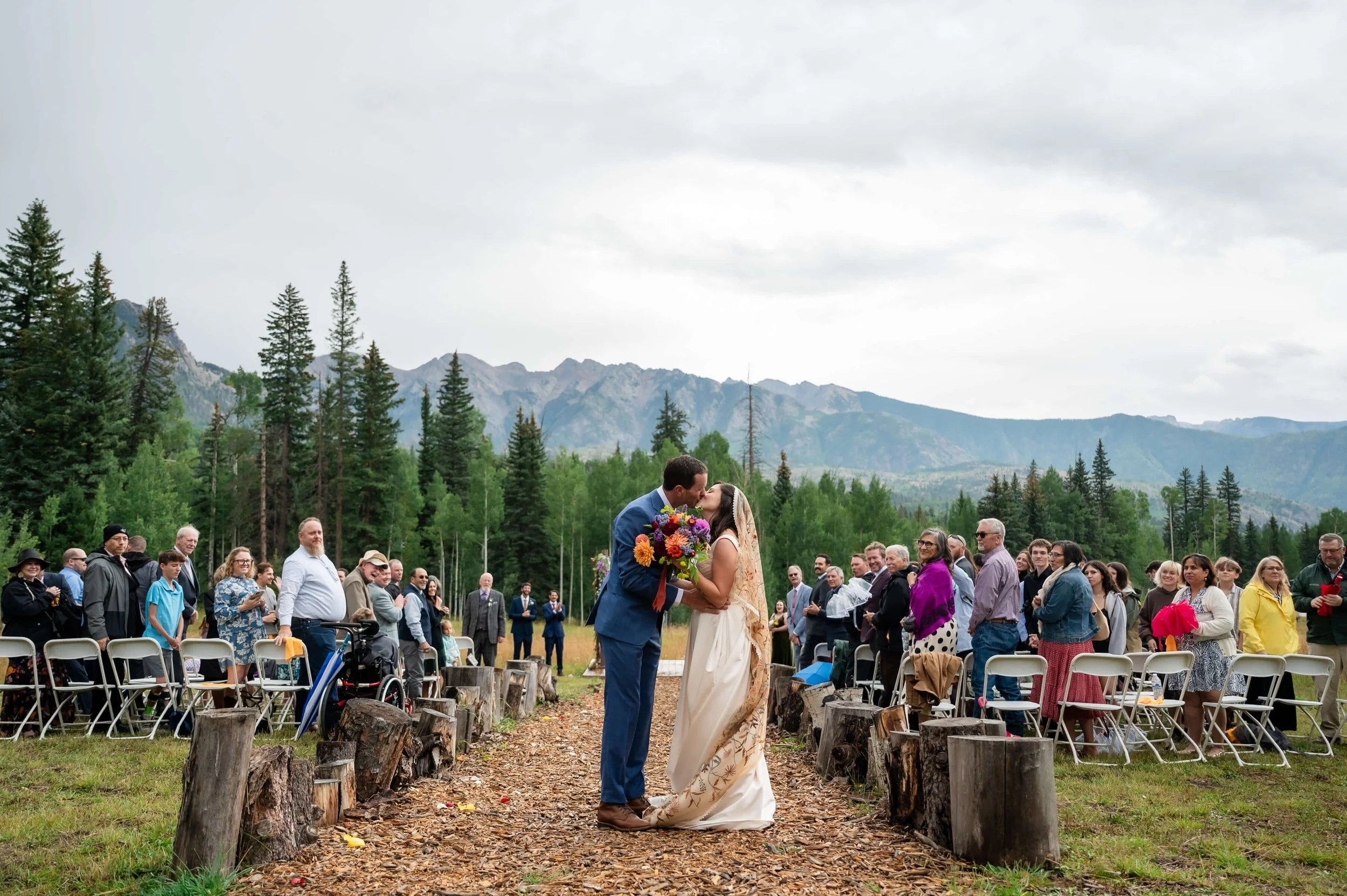 Couple exchanging vows under umbrellas during a rainy outdoor ceremony at The Benchmark at Cascade Village, with fog rolling over the San Juan Mountains.