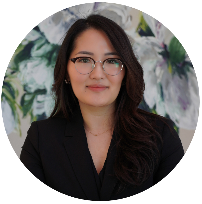 A woman with glasses and dark hair, wearing a black blazer, smiling in front of an abstract floral background.