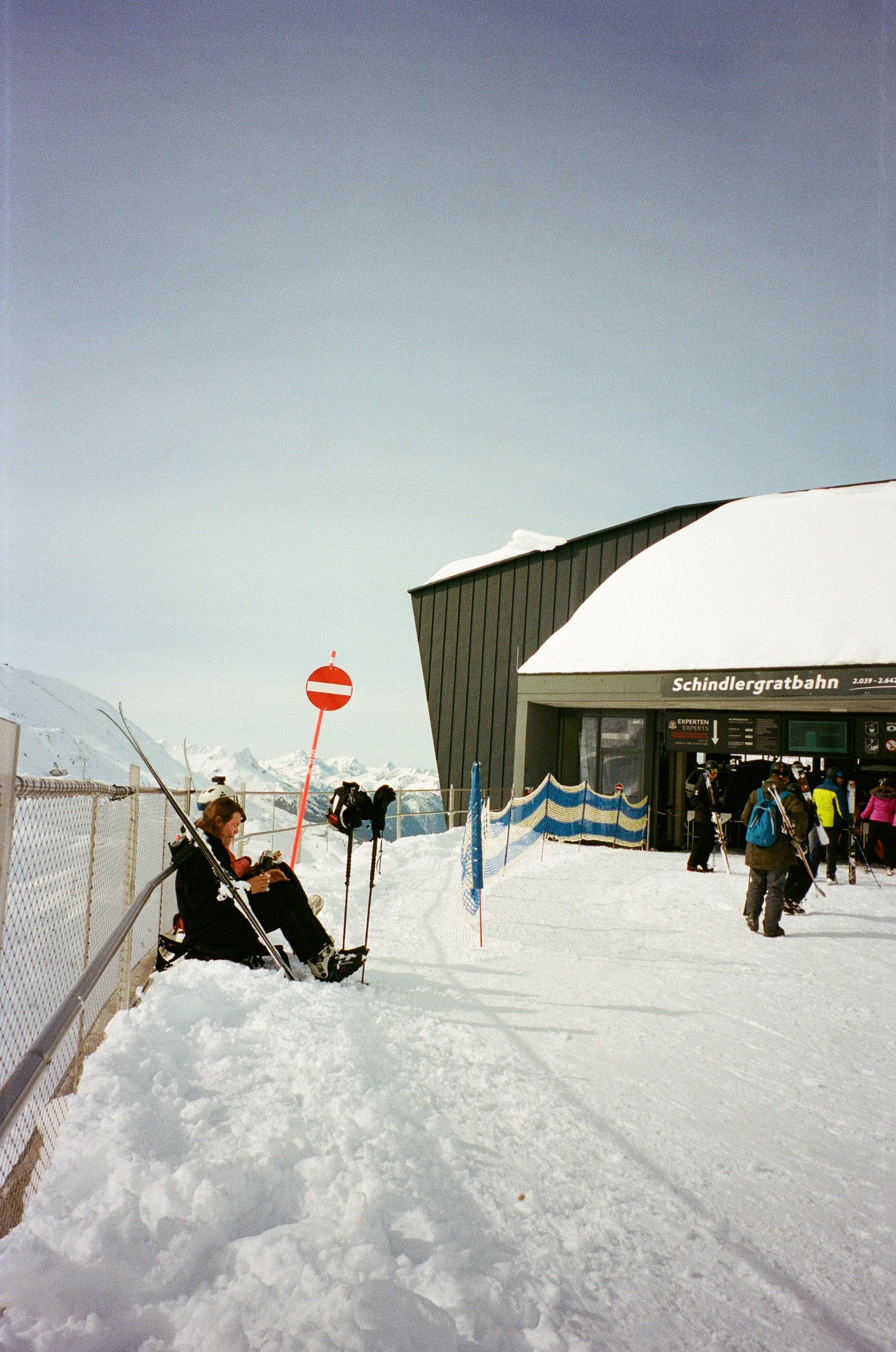 People waiting in line at the Schindlergratbahn ski lift station in a snowy mountain area with clear skies.