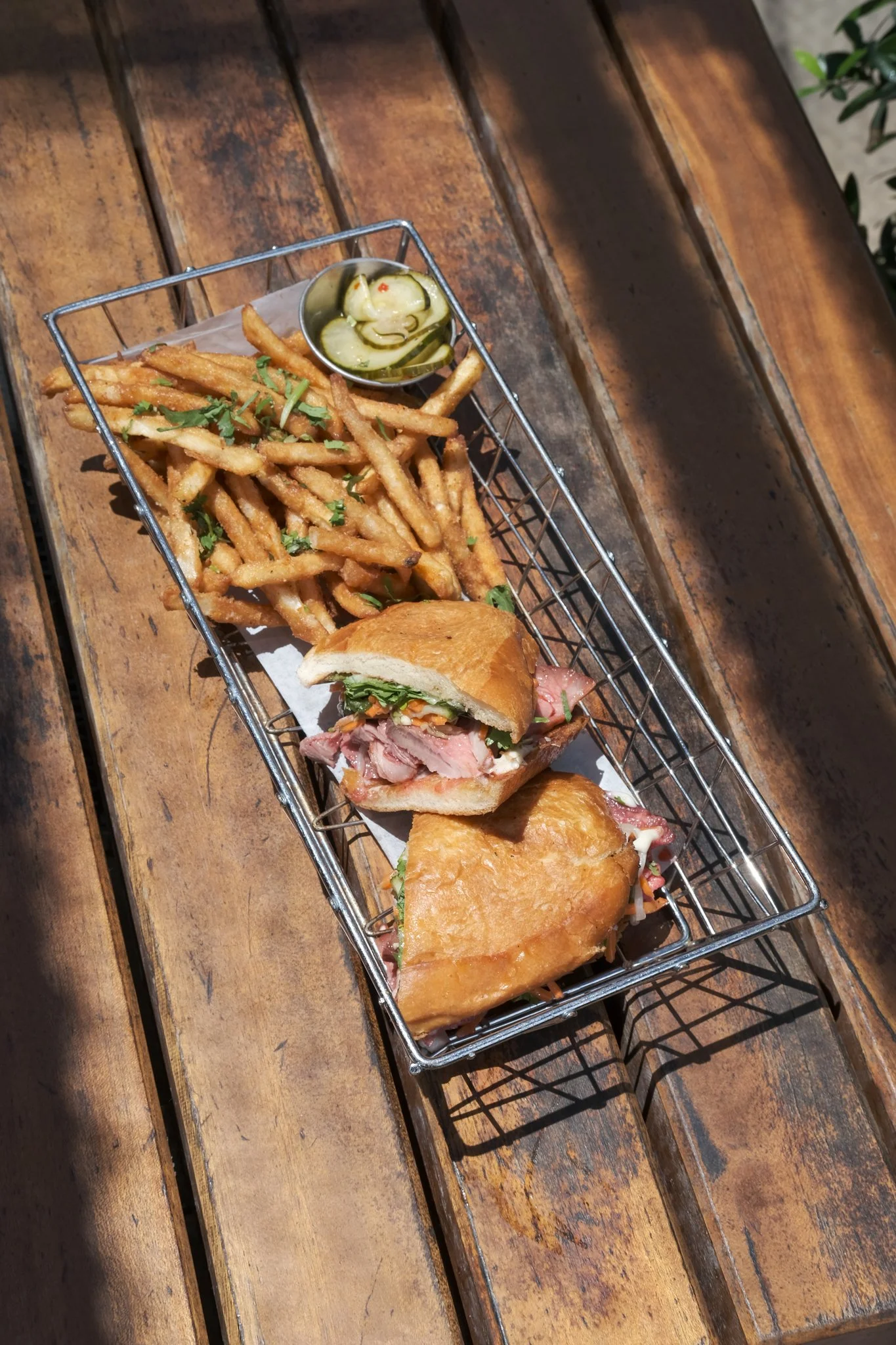 French fry, pickle, and sandwich served on a metal tray on a wooden table.