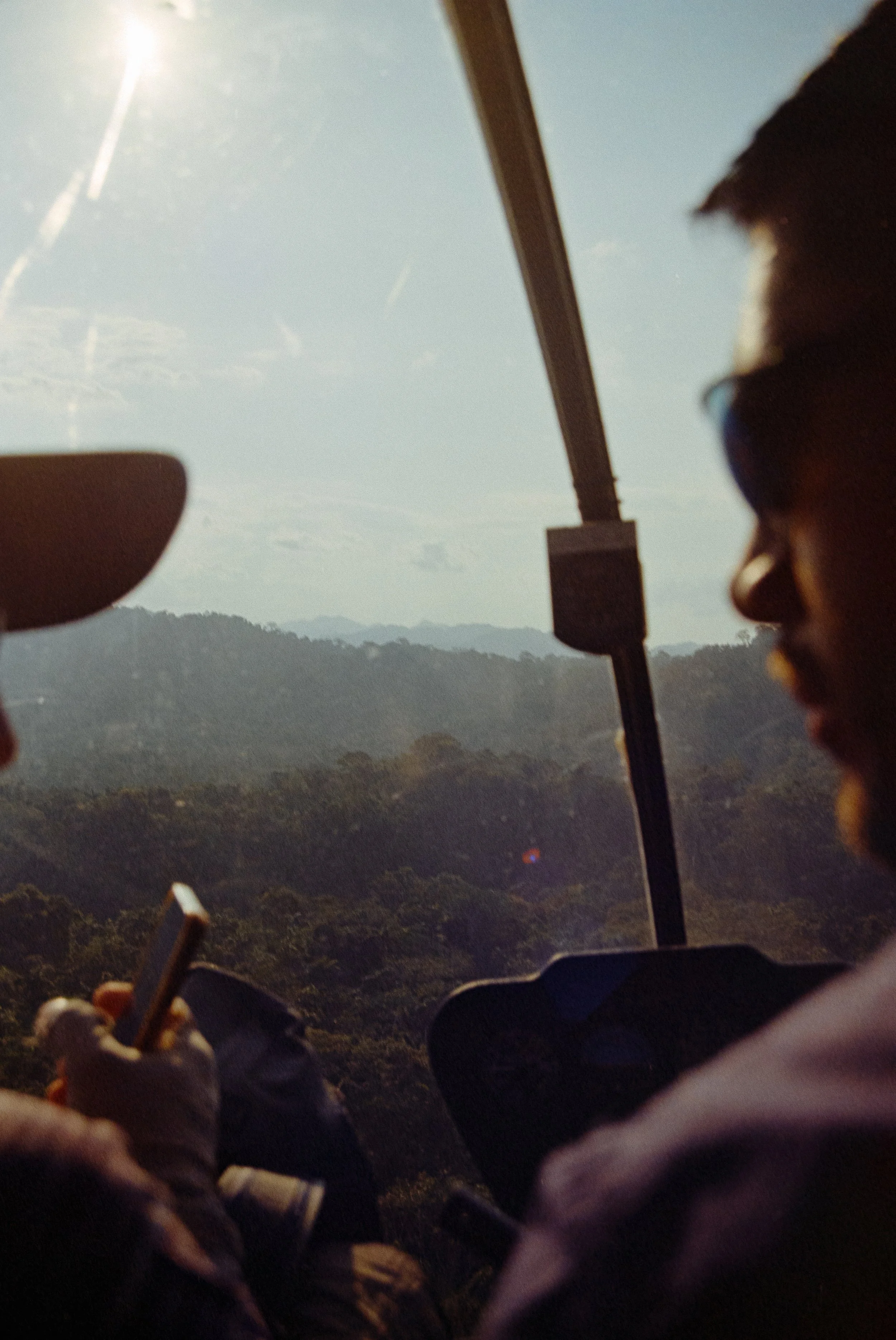People riding a cable car over a forested landscape with mountains in the distance and a clear sky.