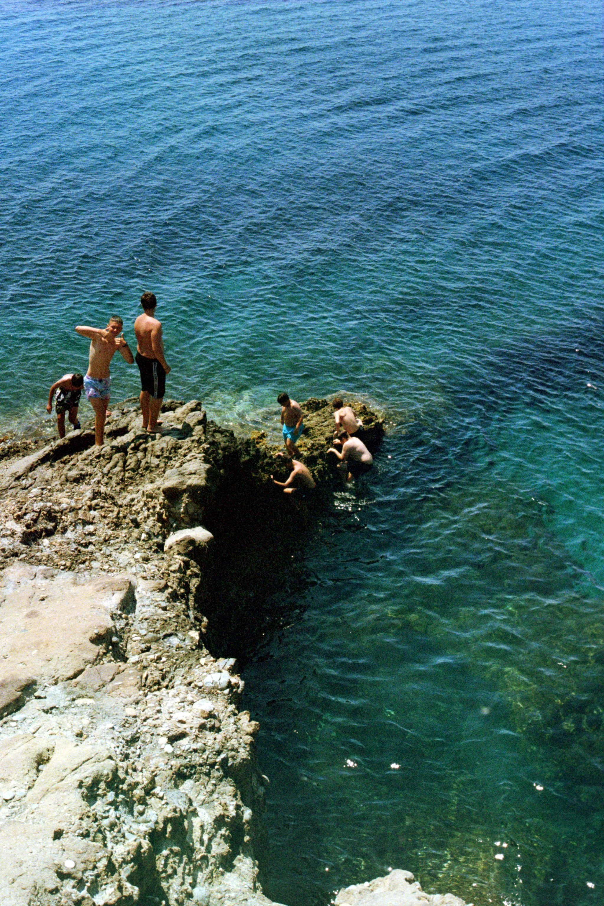 People swimming and relaxing on rocks by the ocean on a sunny day.