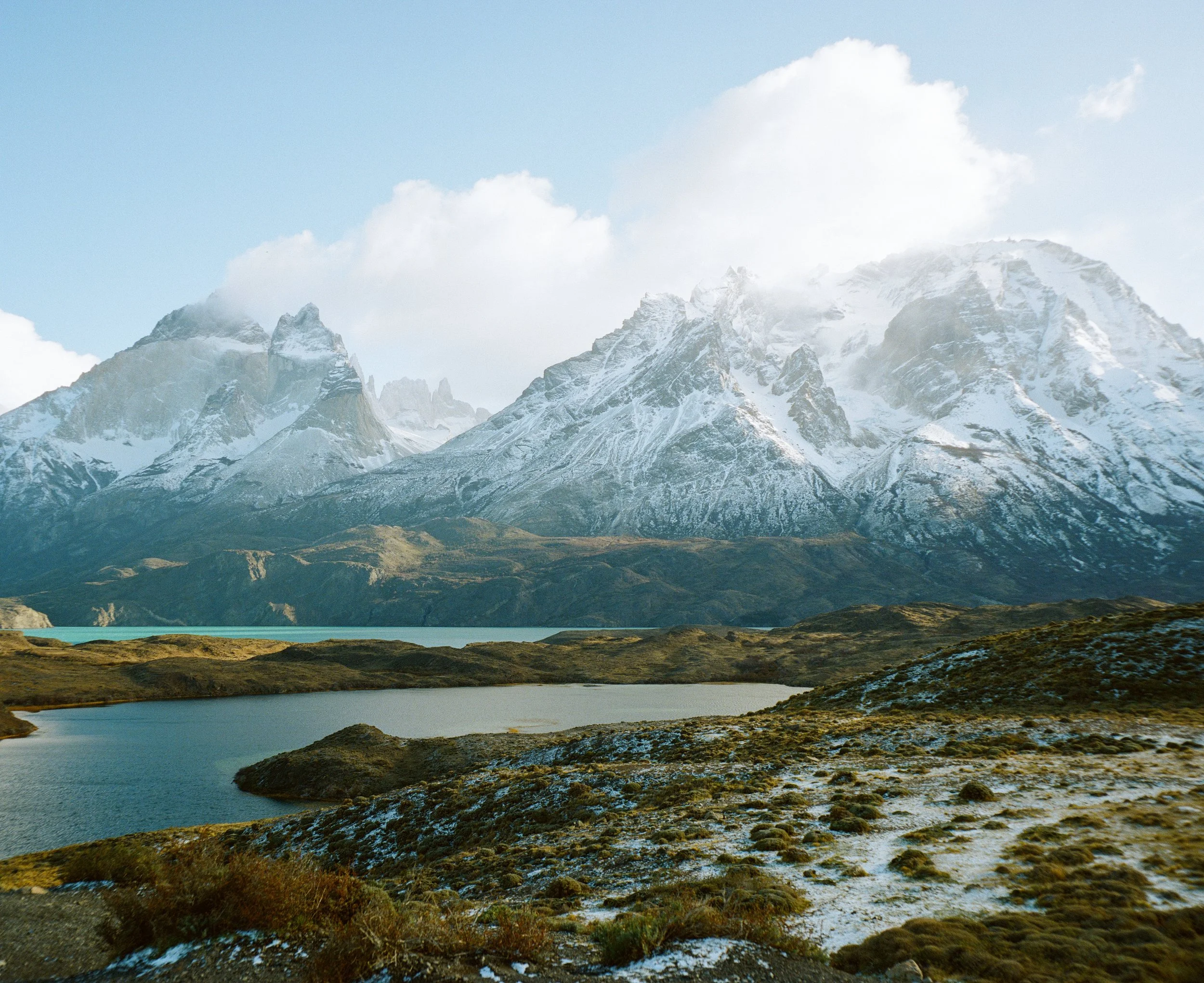 Snow-capped mountains behind a lake and rolling terrain with sparse vegetation.