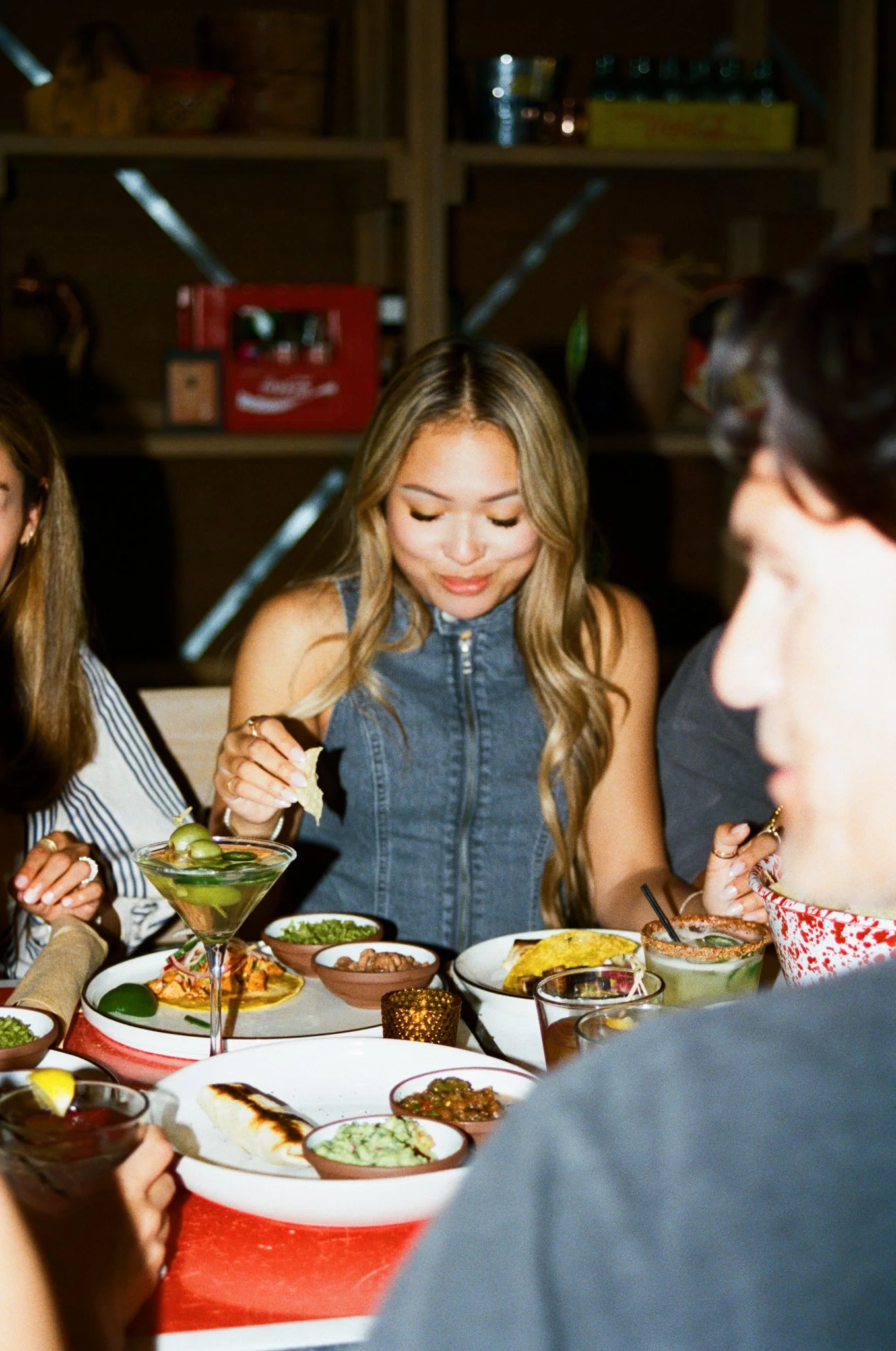 A group of people enjoying a meal together at a table filled with various dishes and drinks in a cozy, rustic restaurant.