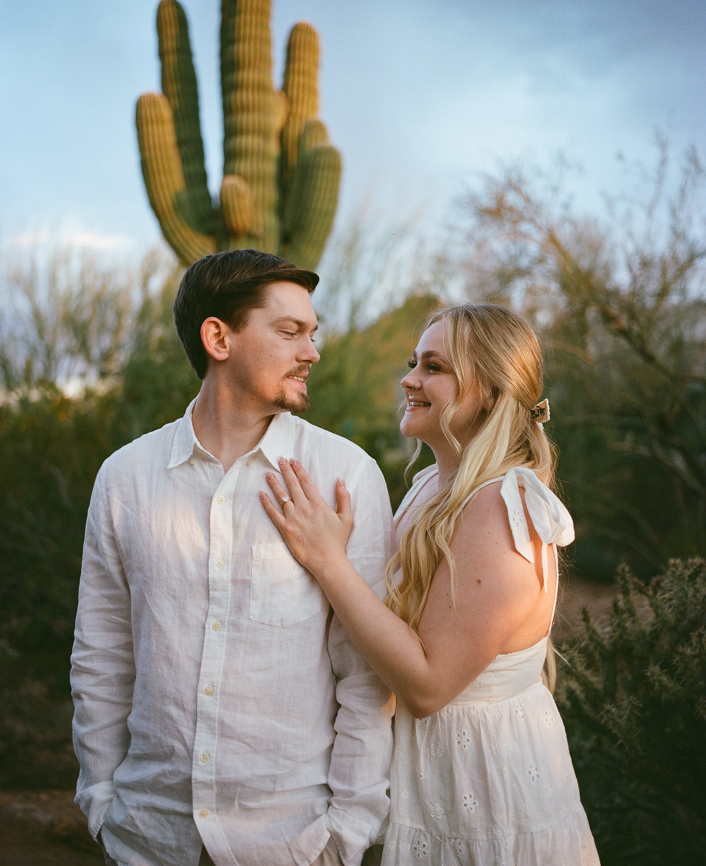 A couple looking at each other outdoors during sunset, with a large cactus in the background.