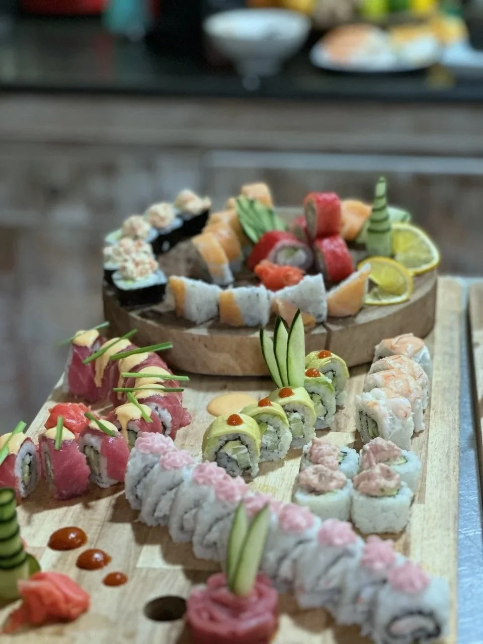 Assorted sushi rolls with various ingredients, garnished with cucumber, lemon slices, and decorative toppings on a wooden serving board.