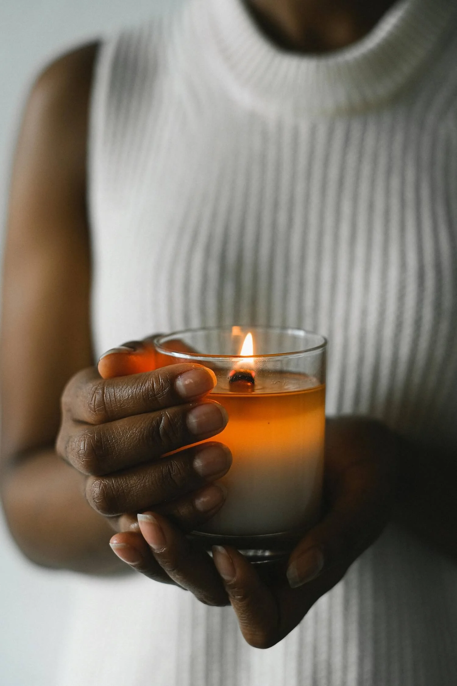 Lit candle held gently in someone’s hands, representing remembrance, warmth, and the steady light we seek during times of grief.
