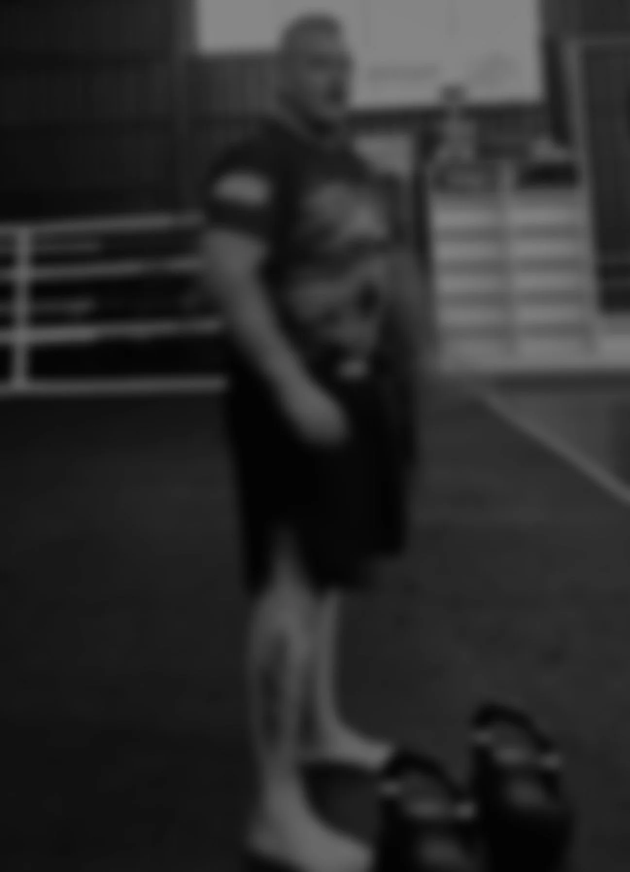 A person standing on an indoor sports court, wearing casual clothes, with a pair of sandals on the ground nearby.