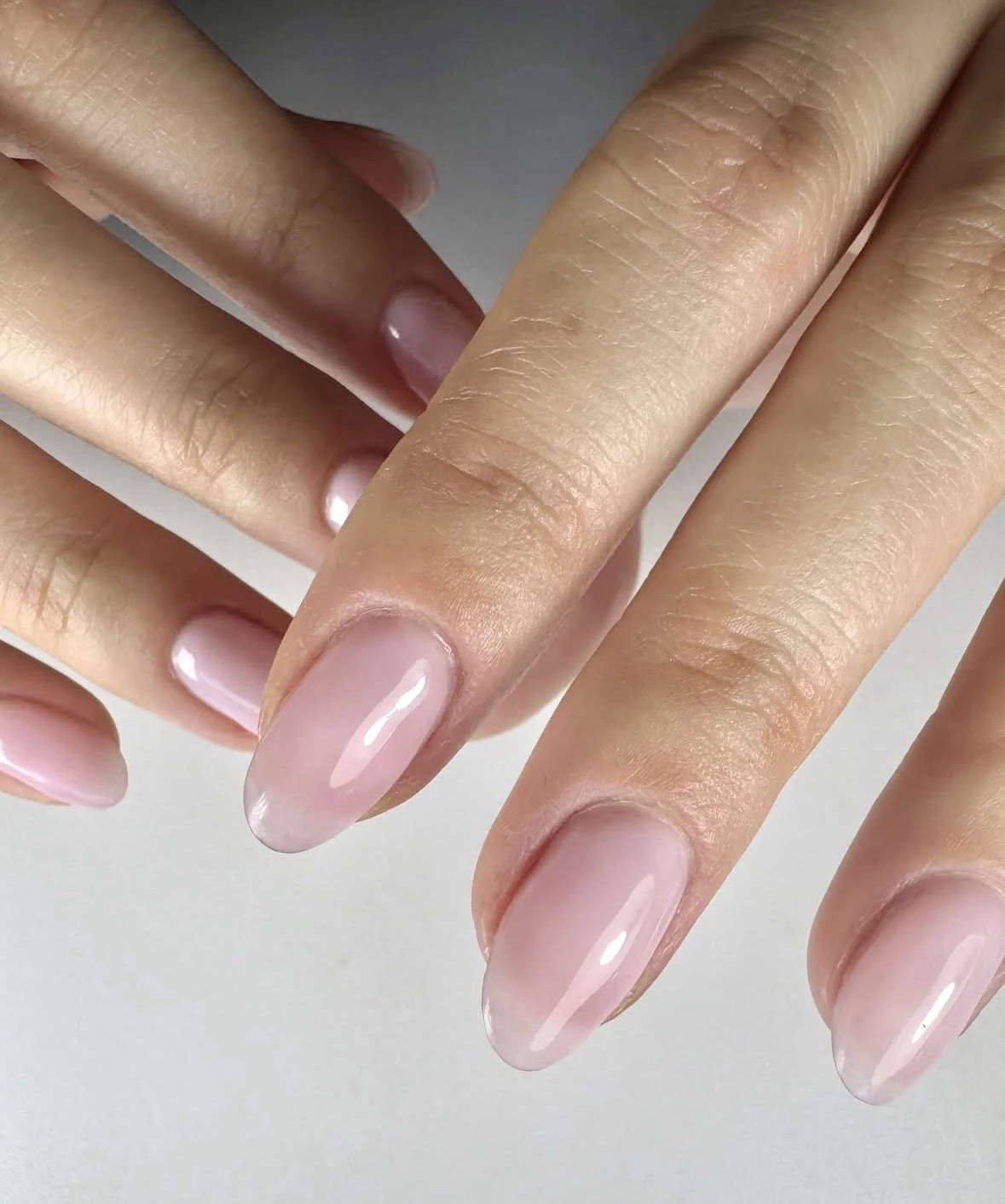 Close-up of hands with well-manicured nails painted in light pink, showing smooth skin and shiny finish.