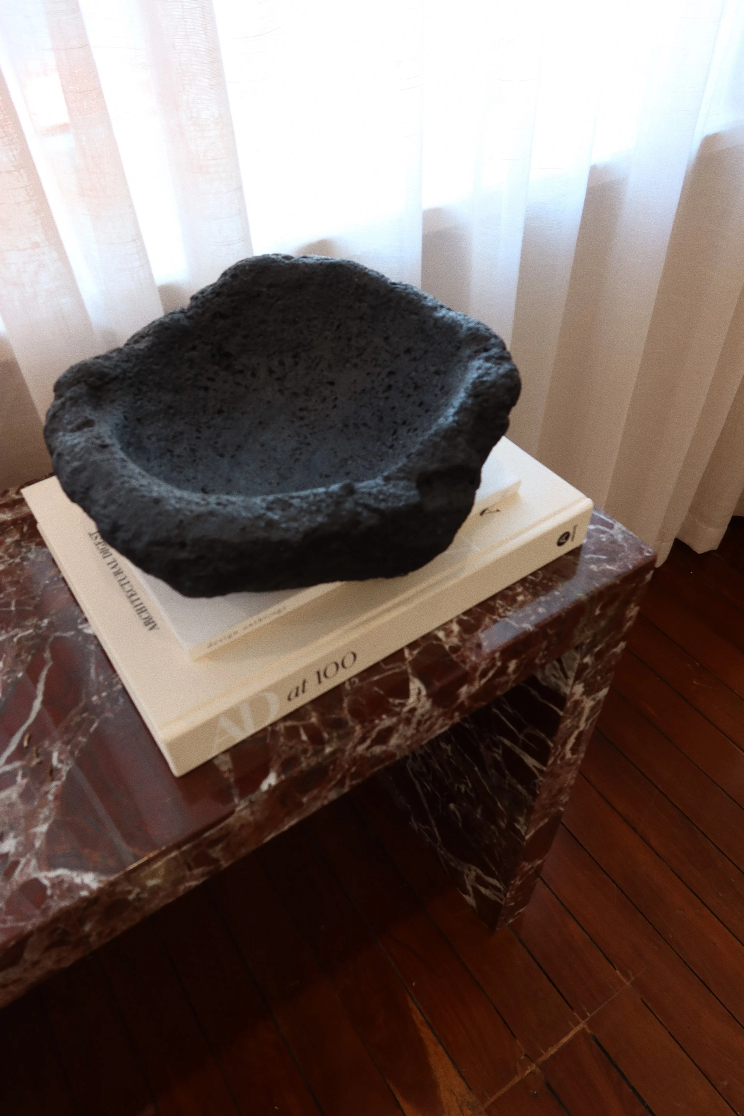 A black volcanic rock bowl resting on a stack of white books on a marble table.