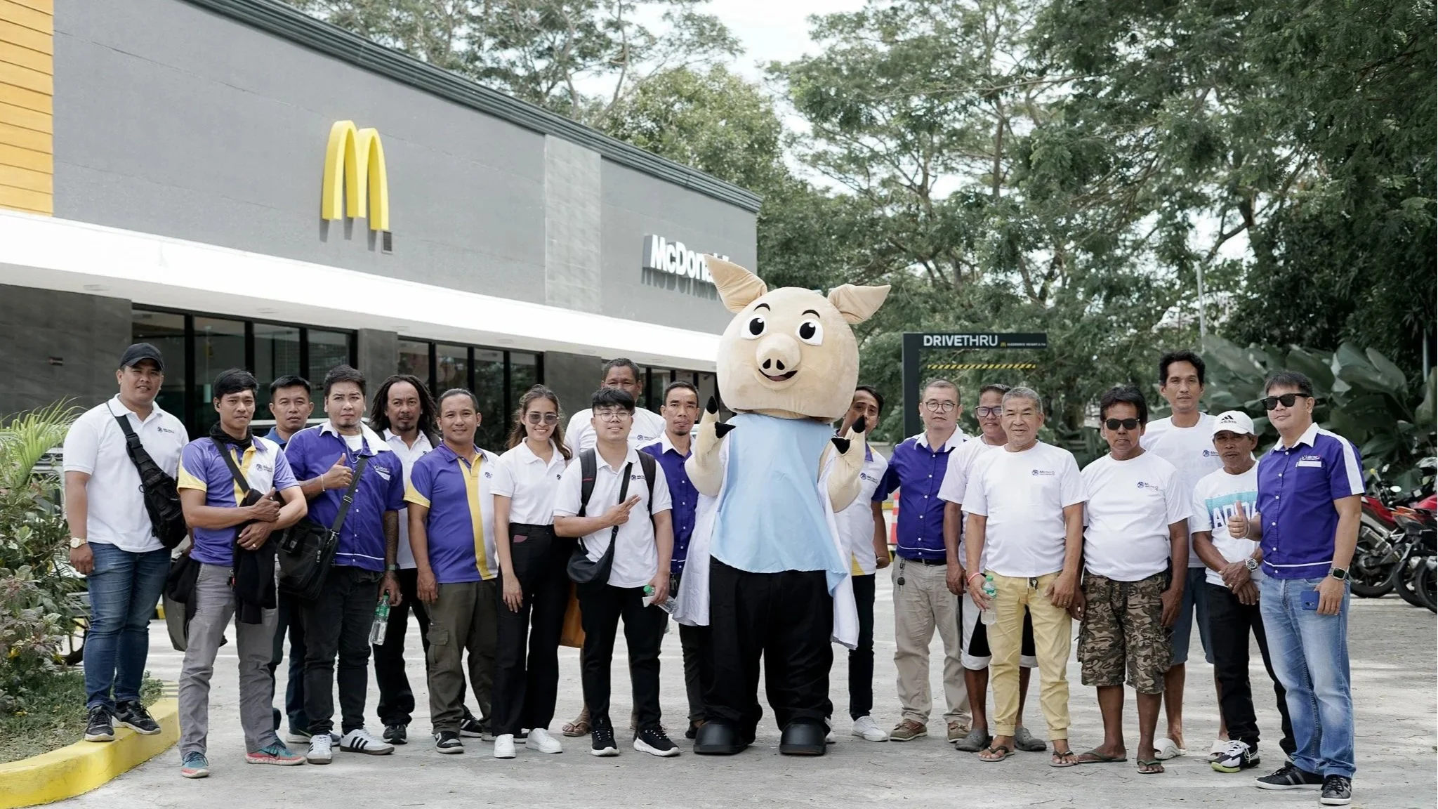 A group of people, including a person in a pig mascot costume, posing in front of a McDonald's restaurant.