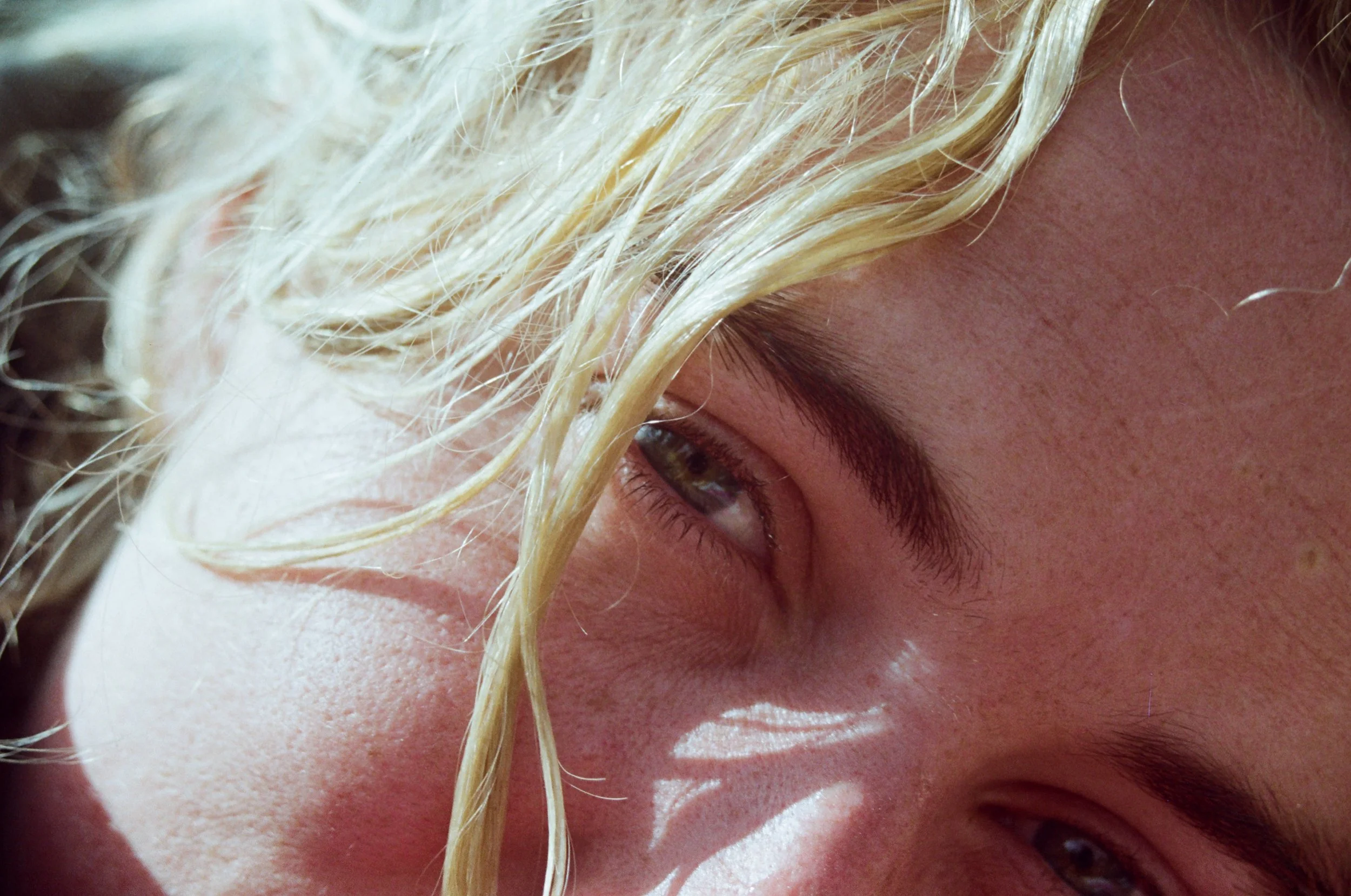 Close-up of a person's face, focusing on their eye, forehead, and blonde, wet hair strand.