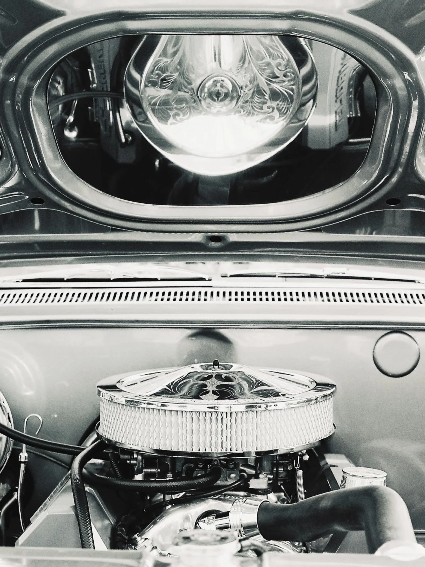 Close-up of a car engine with chrome components and a circular air filter with decorative engravings. The engine bay is clean and well-maintained.