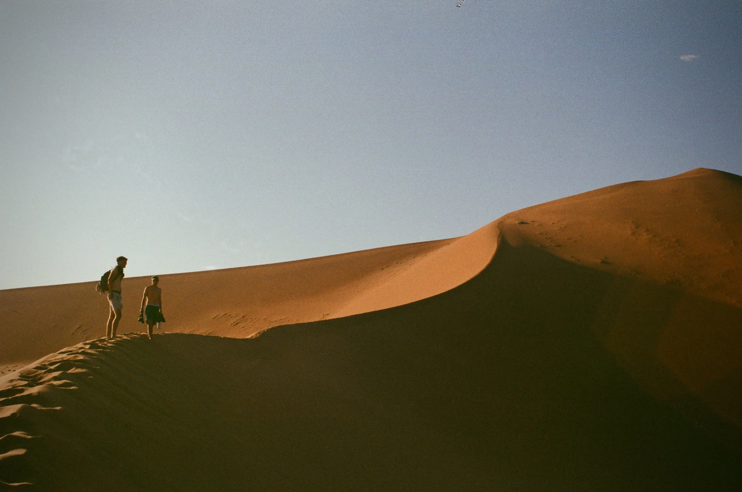 Two people walking on sand dunes in a desert landscape under a clear sky.