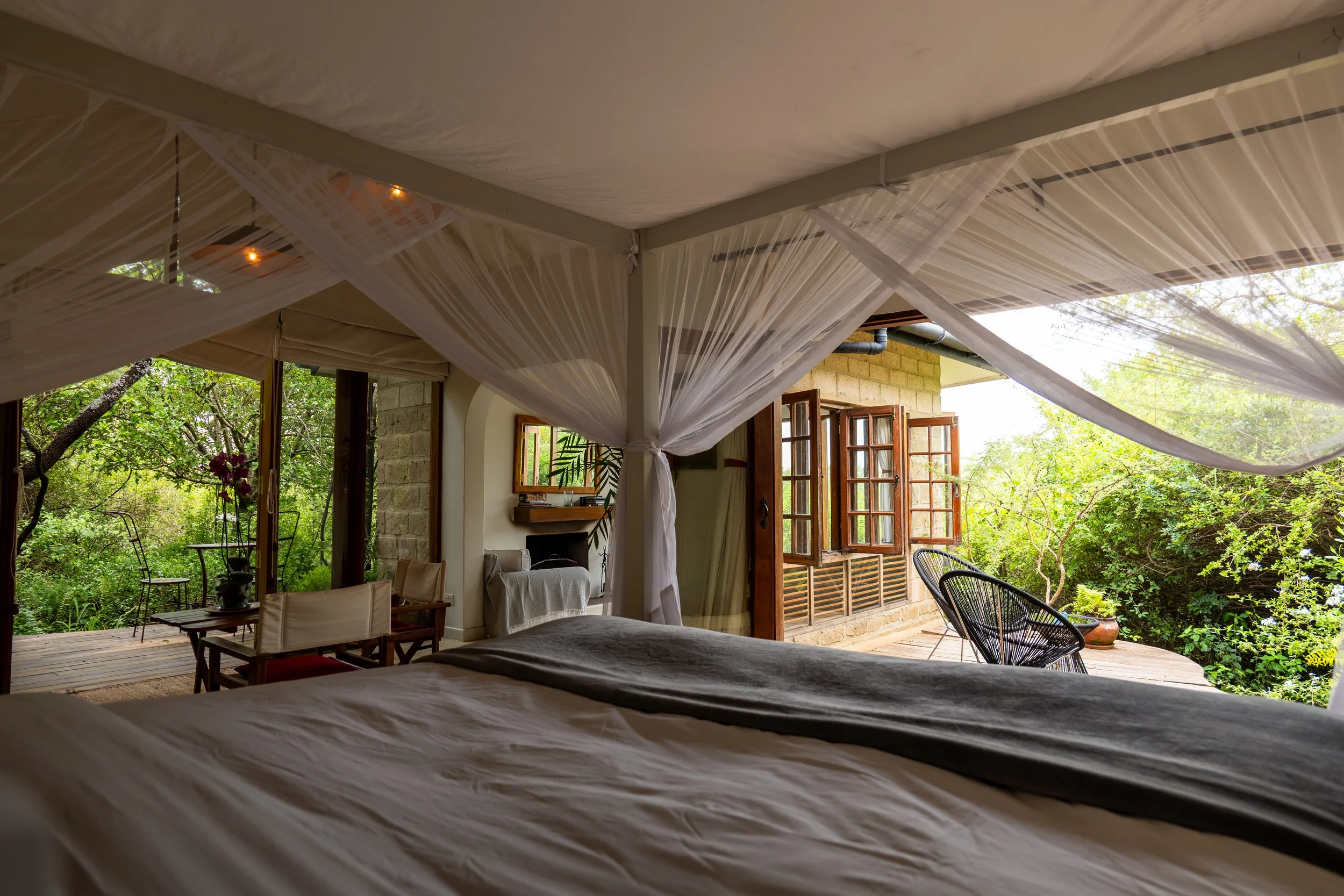 Indoor bedroom with a view of a lush green outdoor patio, decorated with sheer fabric draped and hung across the ceiling.