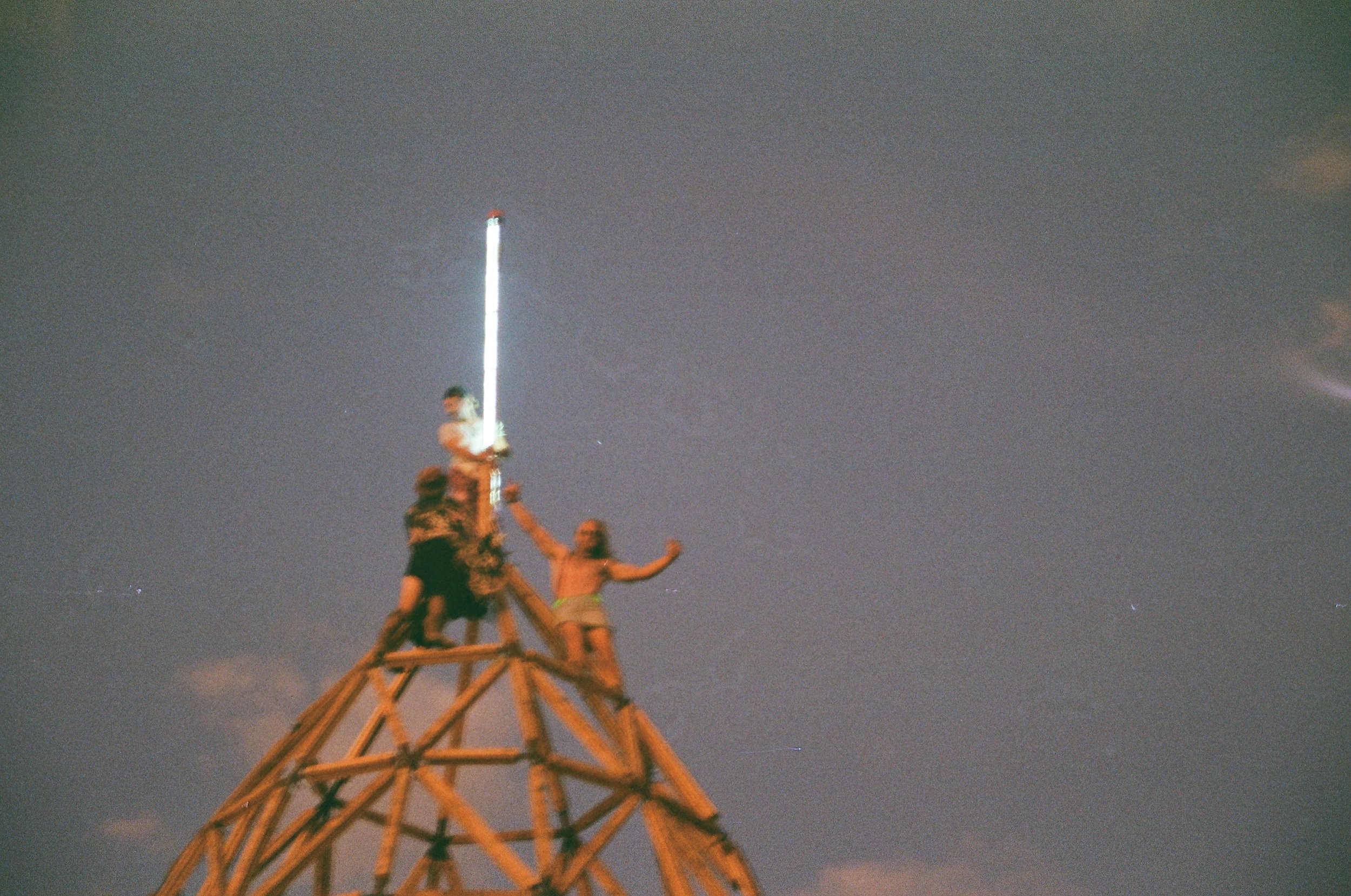 People standing on top of a tower at night, with a bright light or object streaking across the sky above them.