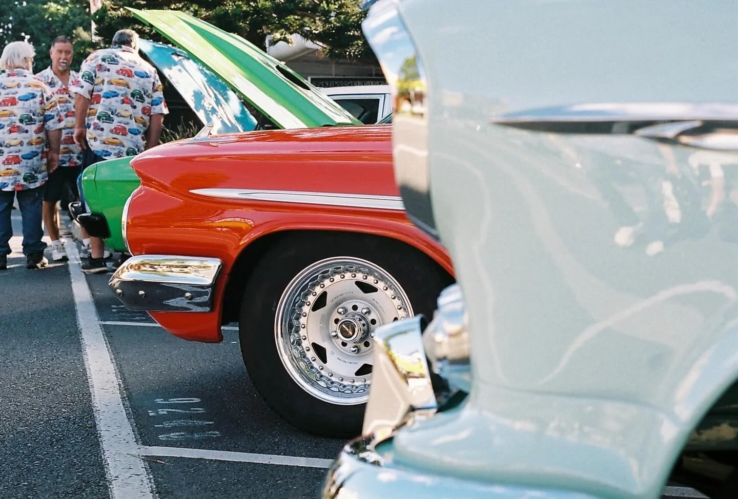 Close-up view of vintage cars parked in a row at a car show, with people in summer shirts in the background