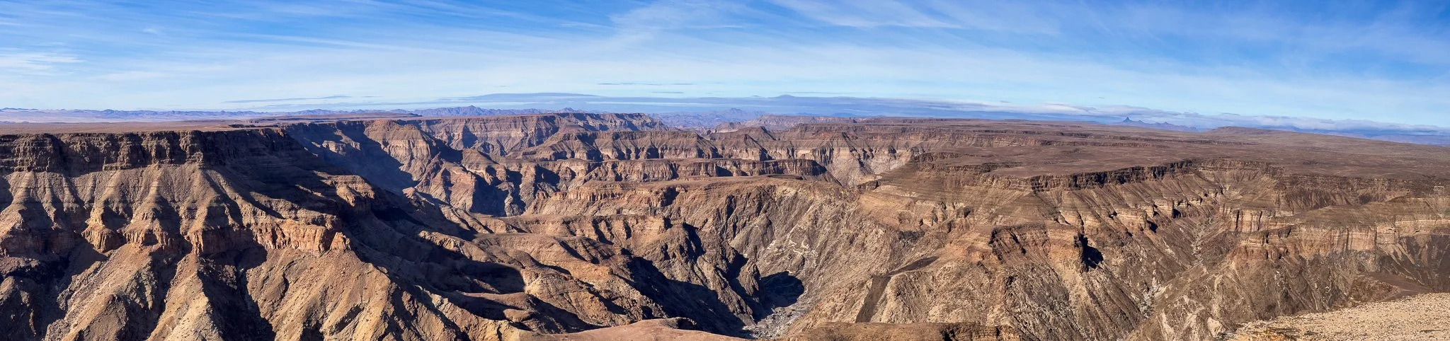 Panoramic view of the Grand Canyon with layered rock formations and a clear blue sky.