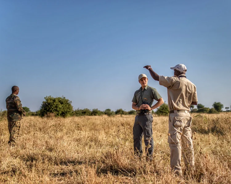 Men standing in a dry grass field, one of them pointing out across it.