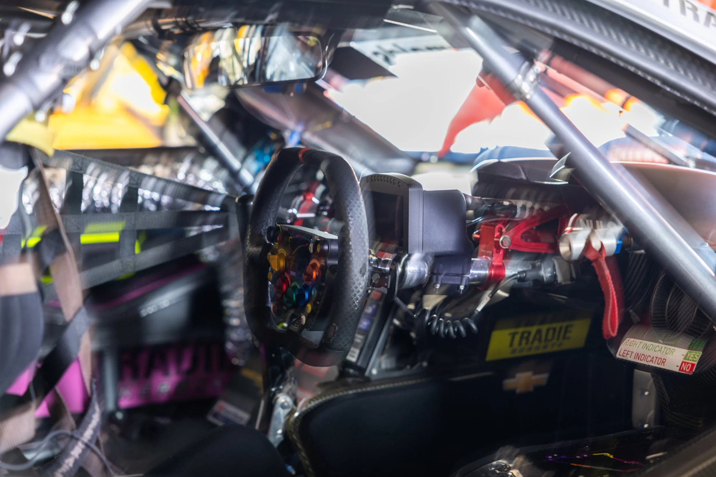 Inside view of a race car cockpit showing a racing steering wheel, digital display, and various wires and electronic components.