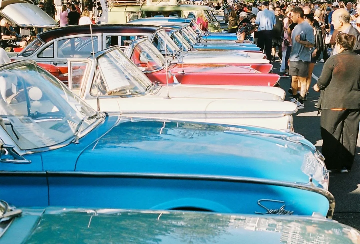 A row of vintage cars on display at a car show with people walking around and observing.