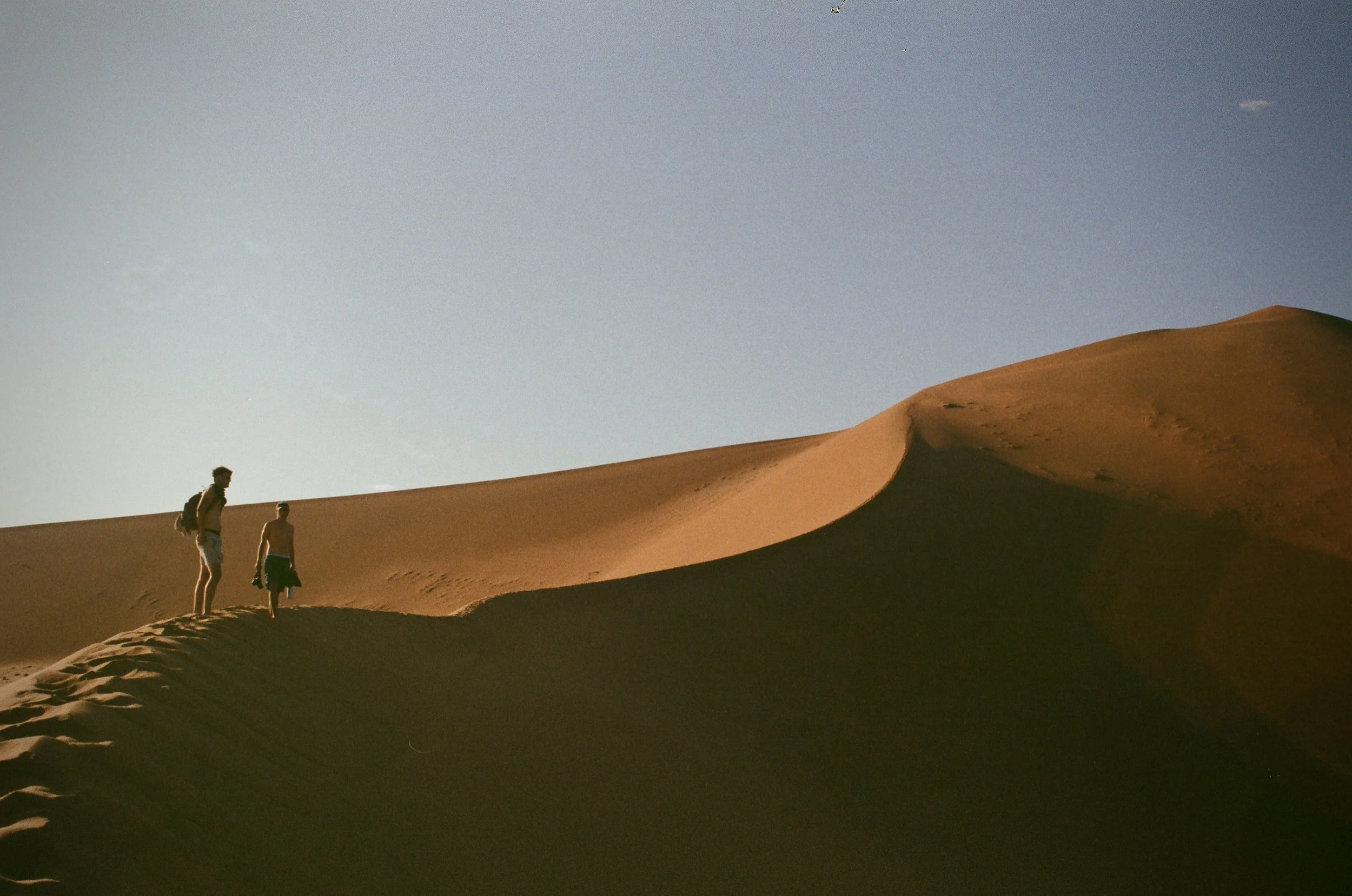 Two people walking on sand dunes in a desert under a clear sky.