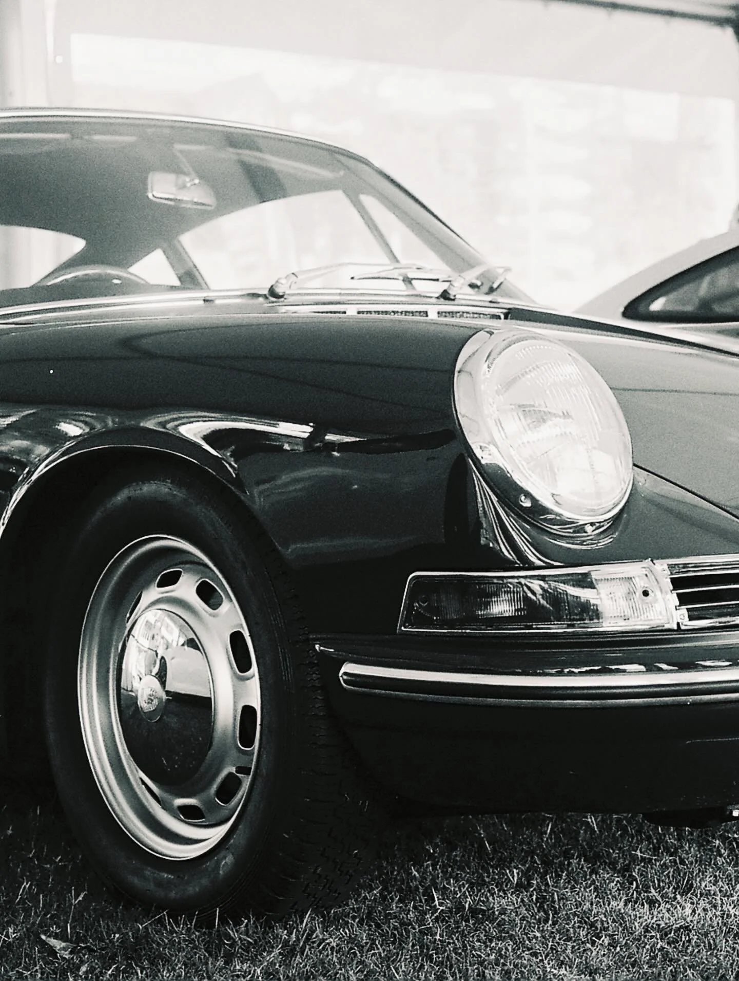 Close-up of the front part of a vintage black Porsche 911 car, showing the headlight, wheel, and front bumper.